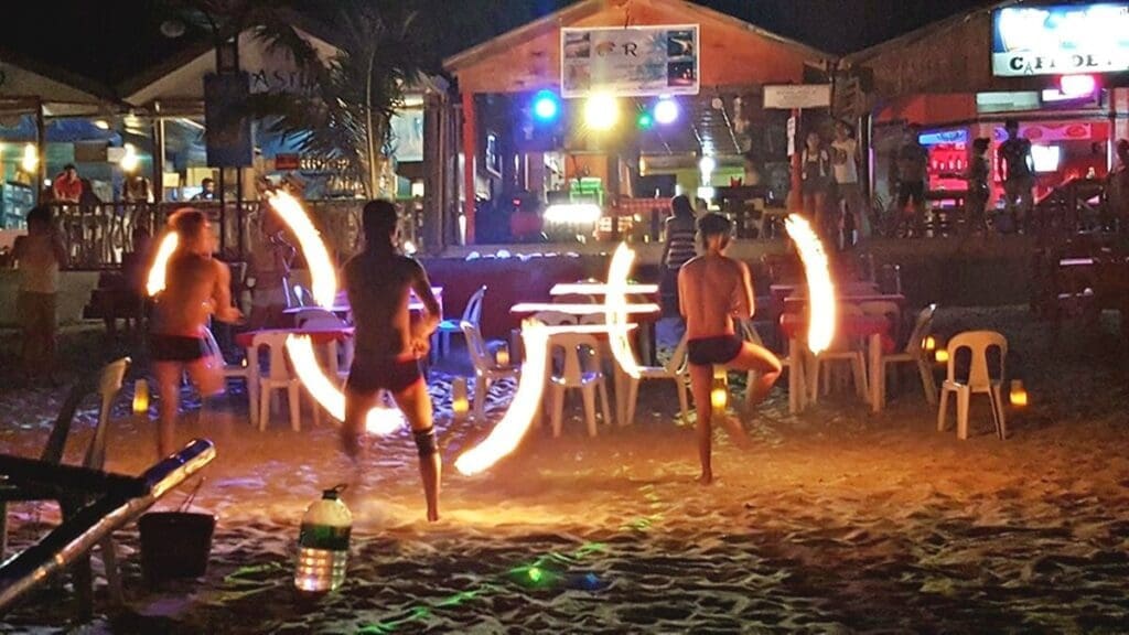 Night market in Puerto Galera with colorful food stalls, fire dancers, and visitors enjoying grilled seafood under string lights.